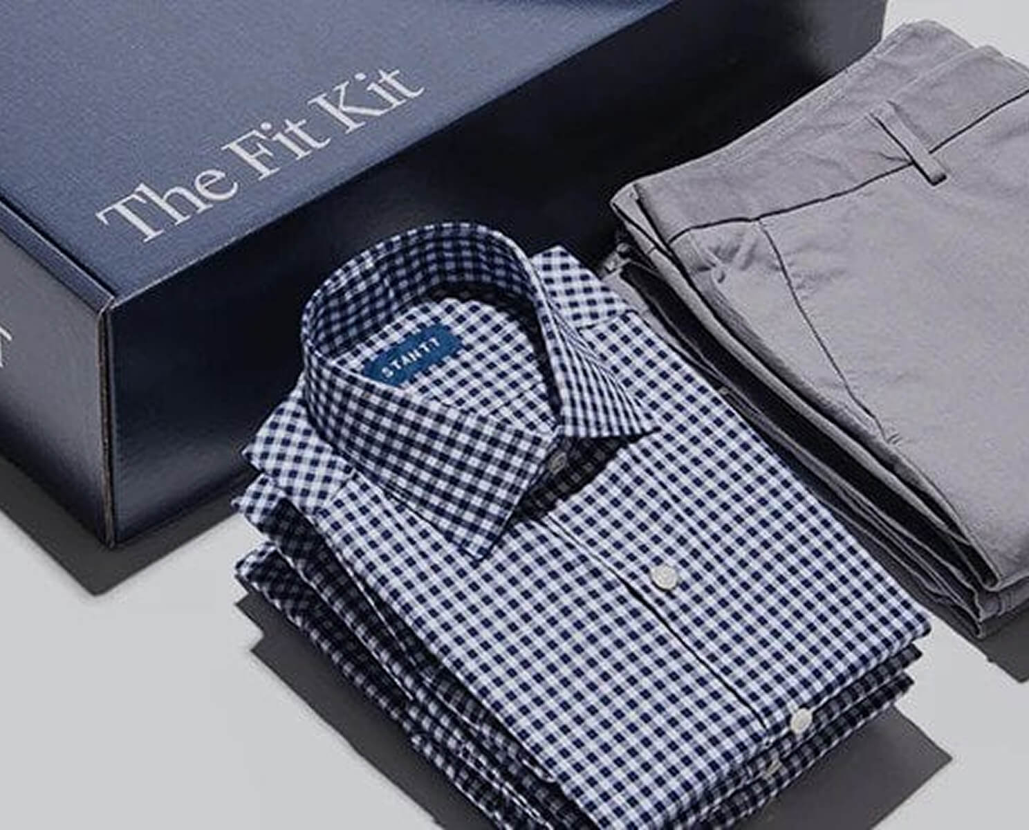 Folded checkered shirt and pants beside 'The Fit Kit' box.