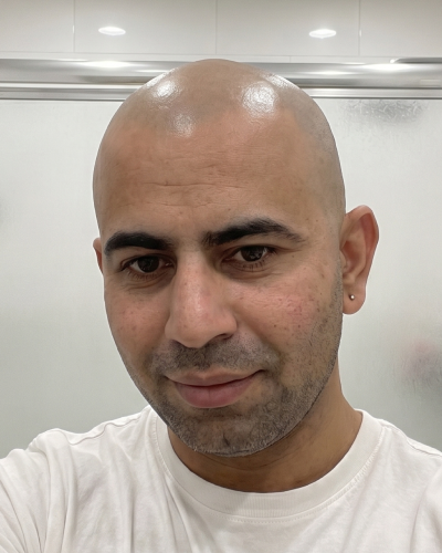 A close-up photo of a smiling man with a shaved head, wearing a white t-shirt and an earring.