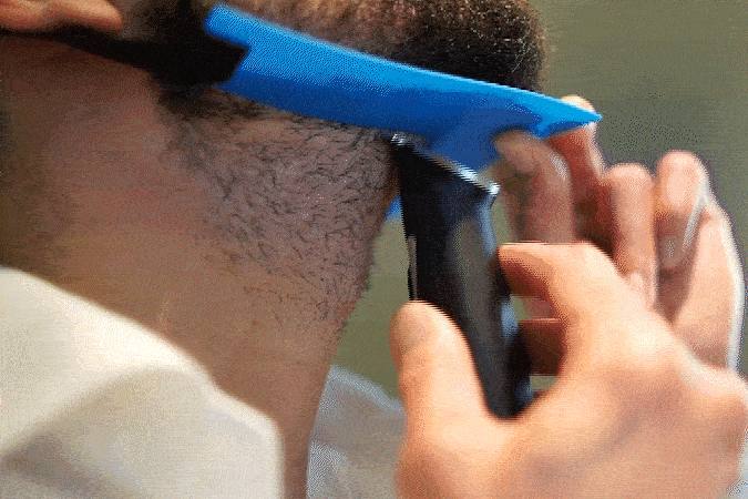 Person using a blue shaving guide and electric trimmer on their beard.