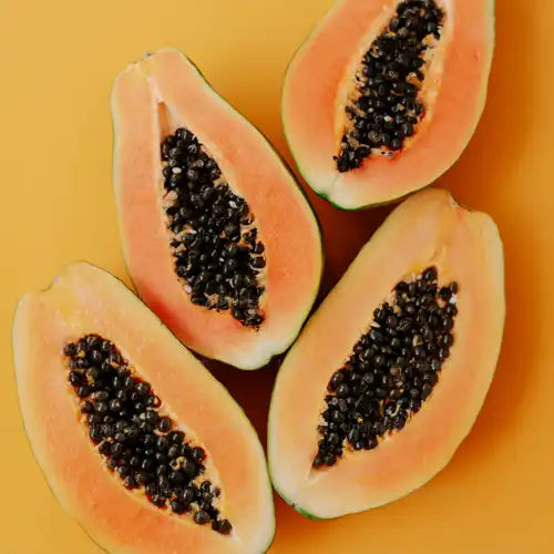 Four cut papayas with seeds on a yellow background.