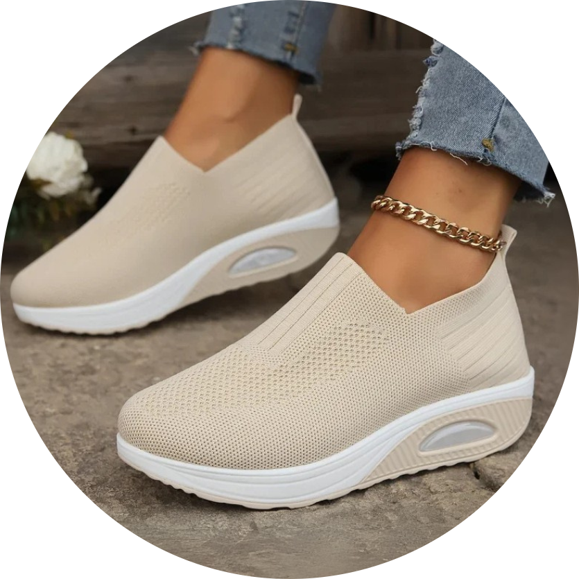 Beige slip-on sneakers with white soles worn with ripped jeans and a gold anklet.