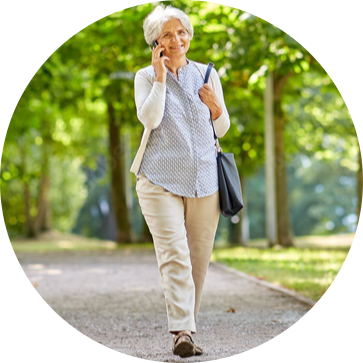Elderly woman walking in a park, talking on a phone.