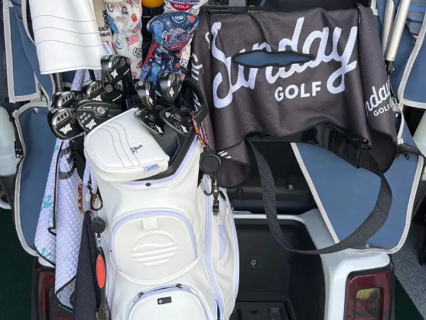 Two golf bags, one white and one black, filled with clubs and towels in a golf cart.