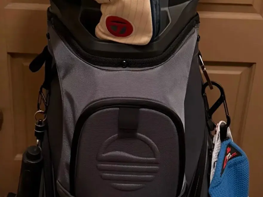 A close-up of a grey and black golf bag with a club headcover and attached towel and accessories.