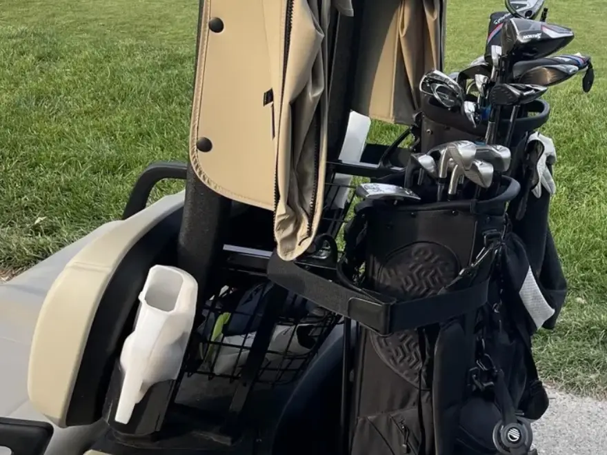 A close-up of a black golf bag with clubs strapped to the back of a golf cart.