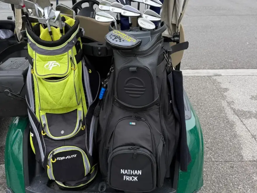 Two golf bags, one lime green and one black, full of clubs on the back of a golf cart.
