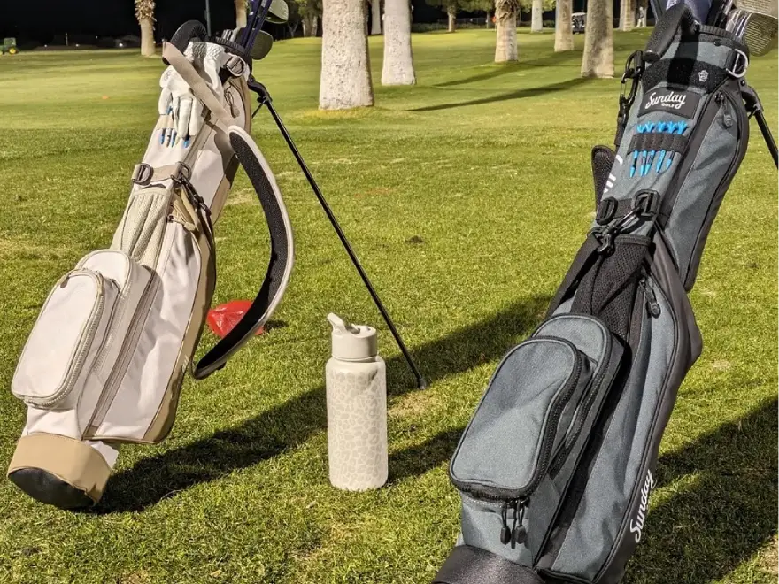 Two golf bags with clubs and a water bottle standing on a golf course at night.