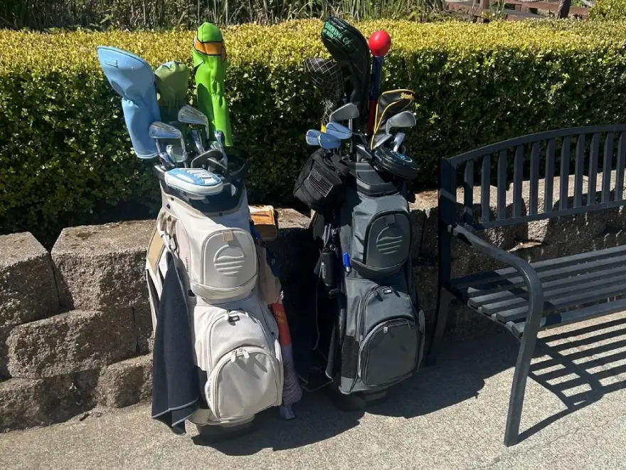 Two golf bags filled with clubs standing on a patio next to a black bench.
