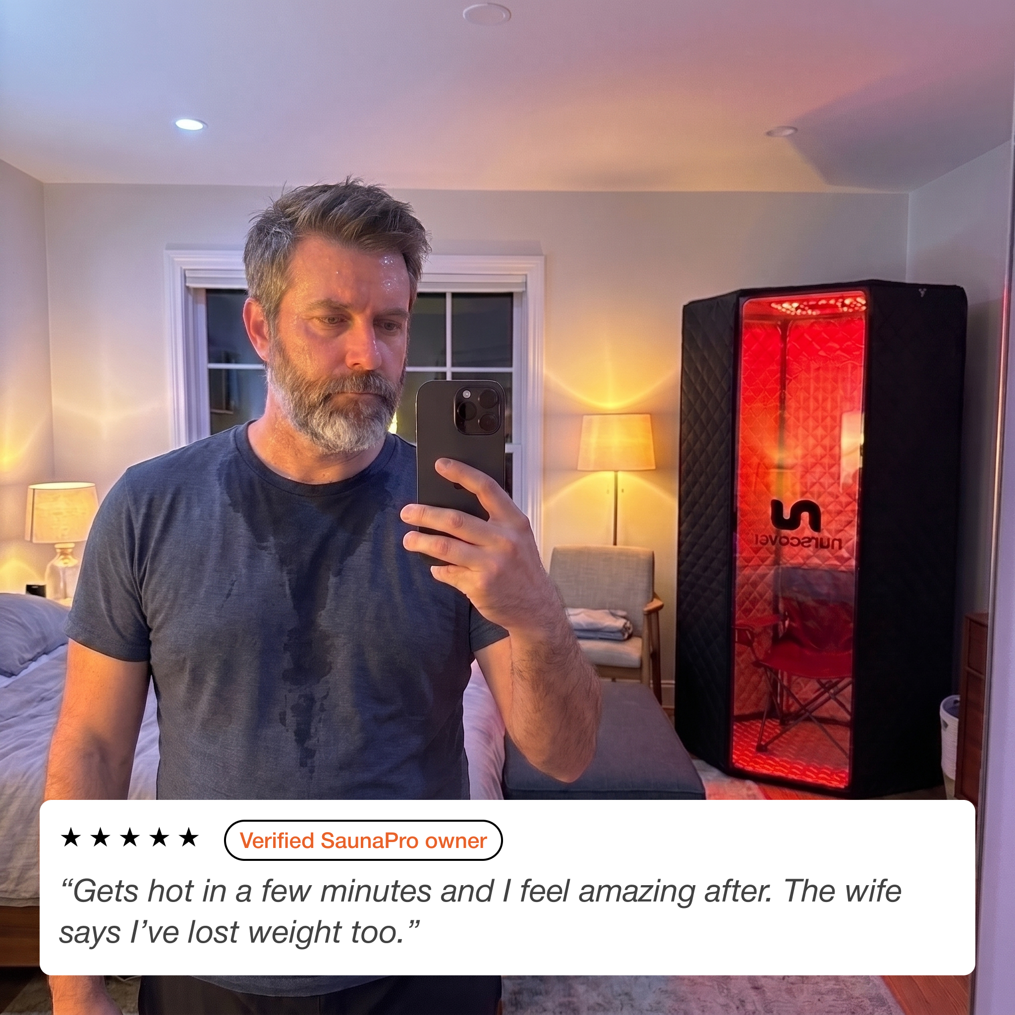 A sweaty man takes a selfie in a bedroom with a portable sauna behind him.