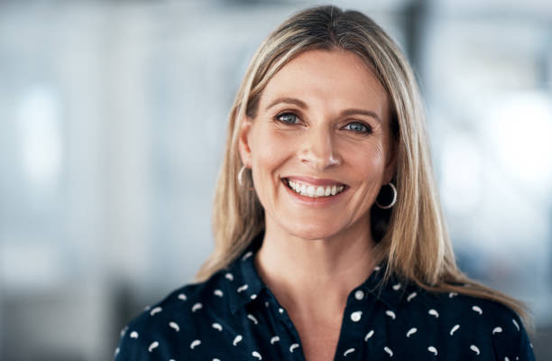 A smiling, middle-aged woman with blonde hair and a dark, patterned blouse.