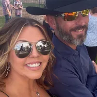 Two people smiling, one wearing sunglasses and another a cowboy hat.