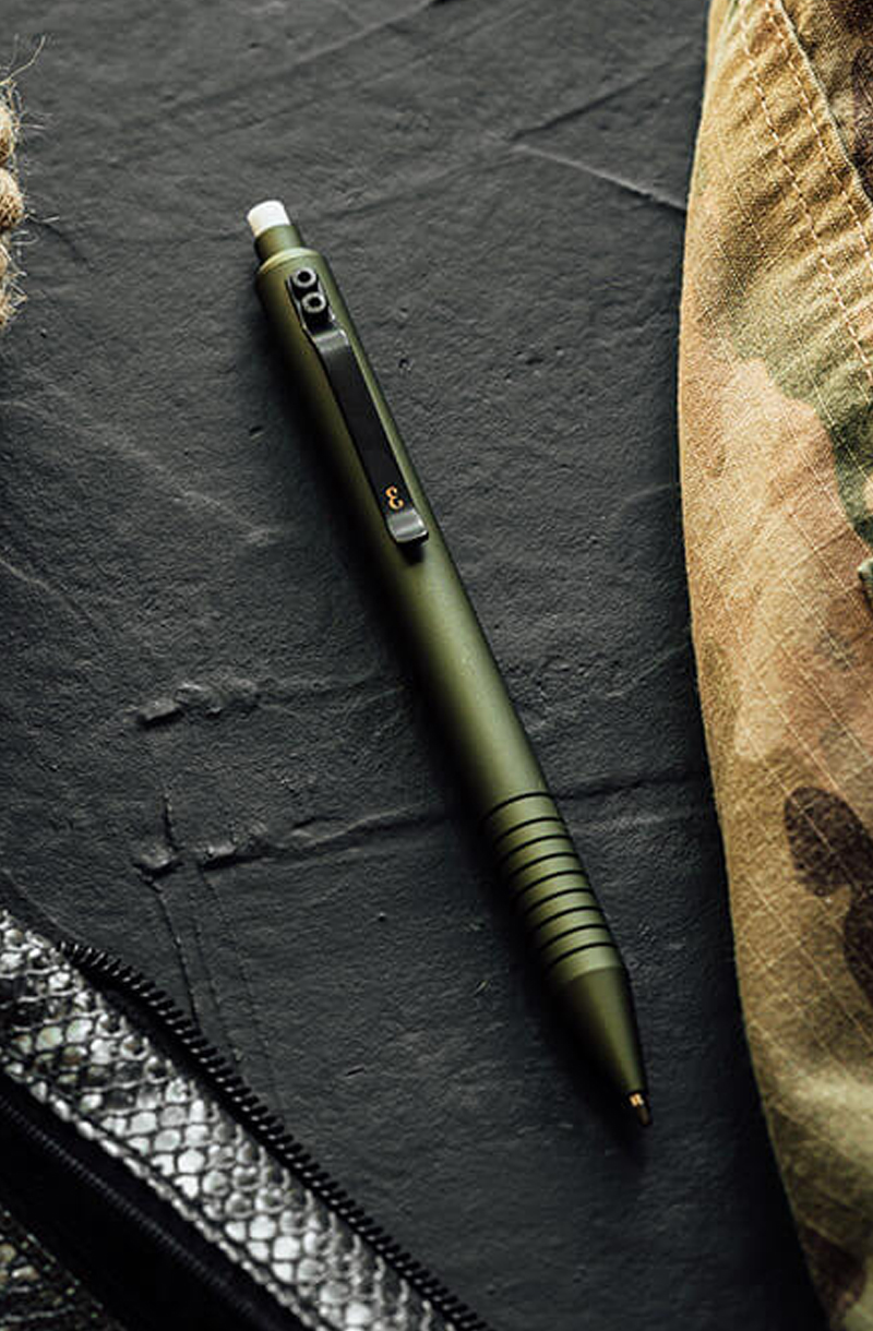 A green pen on a dark textured surface next to a camouflage fabric.