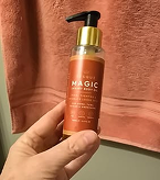 Hand holding a bottle of liquid soap in front of a pink towel.