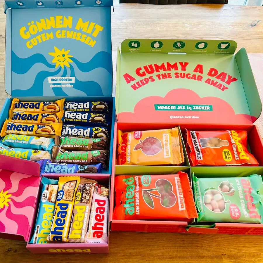 Boxes of assorted protein bars and gummy snacks on a wooden table.
