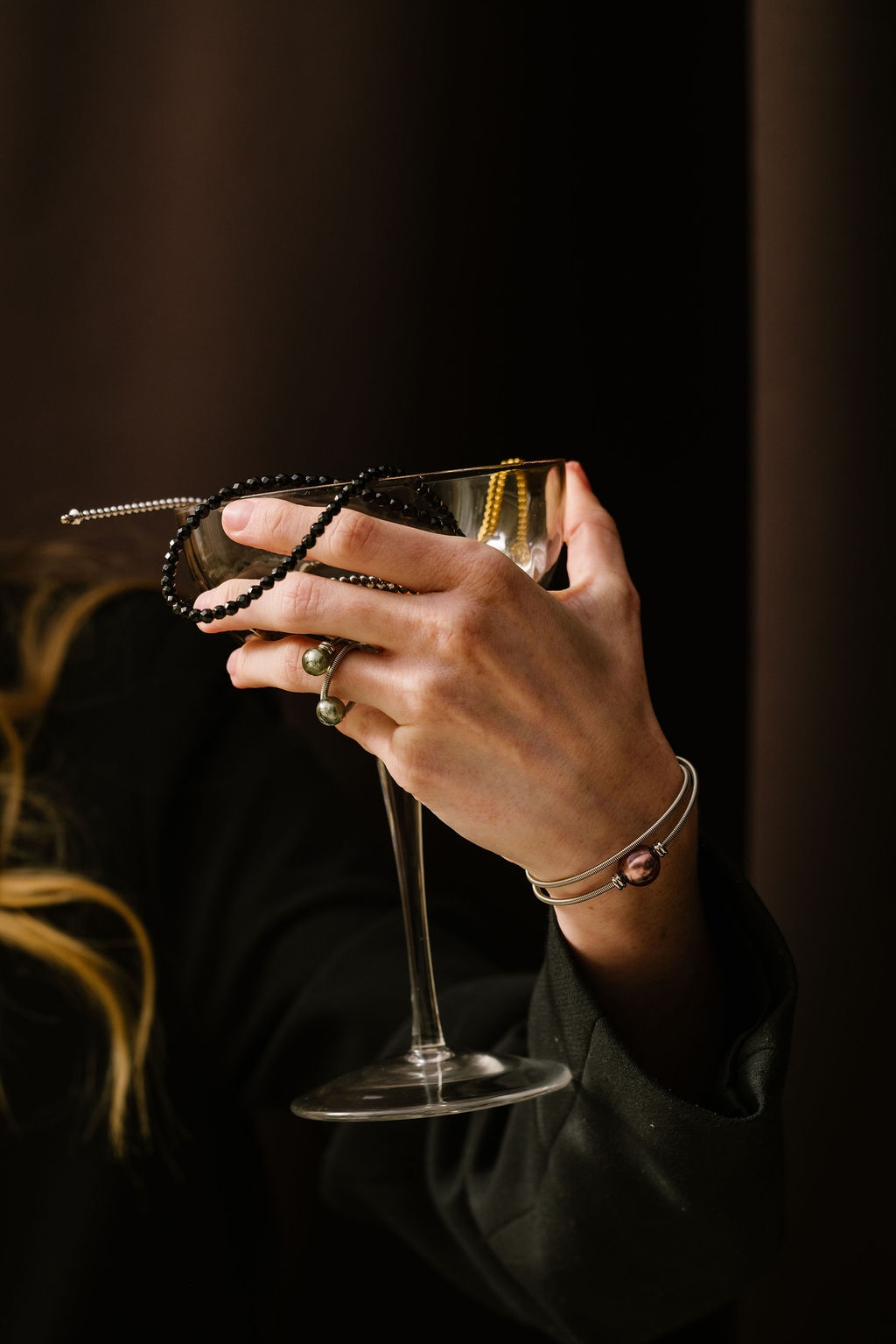 Hand holding a champagne glass with black and gold beads draped over it.