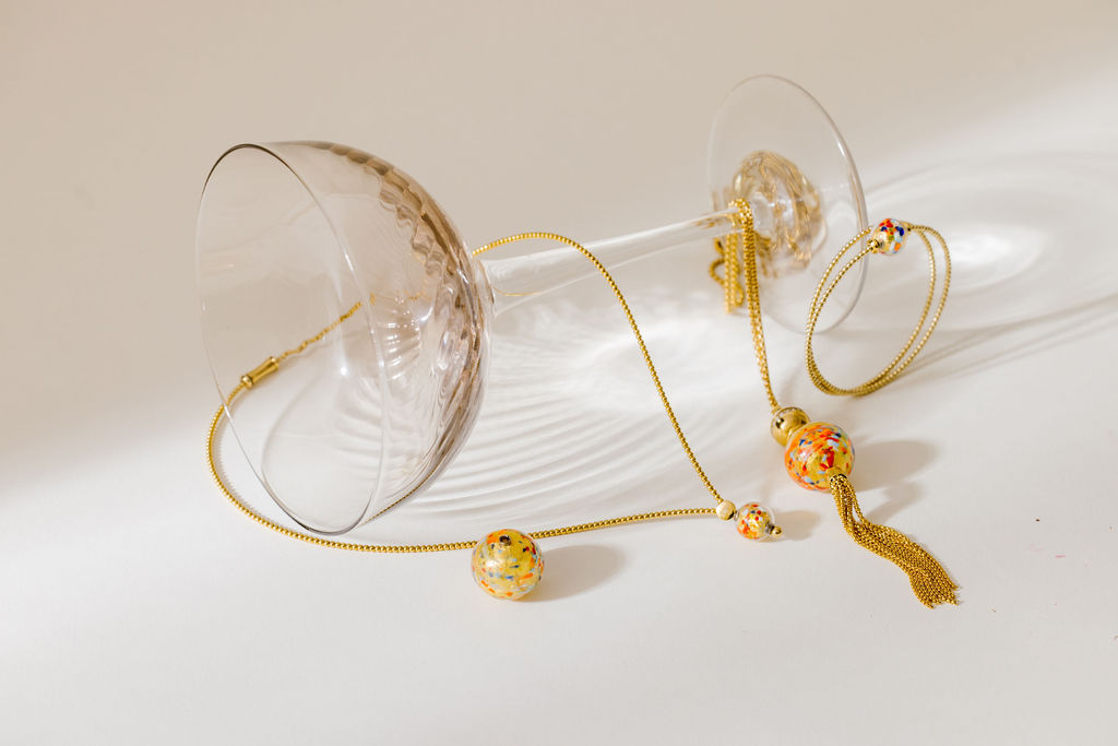 A glass laying on its side with gold jewelry draped around it.