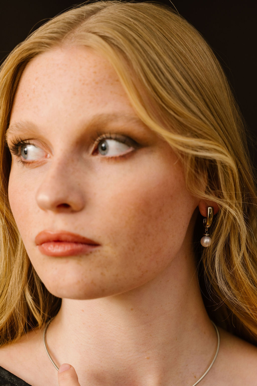 Close-up of a person looking to the side, wearing an earring and necklace.