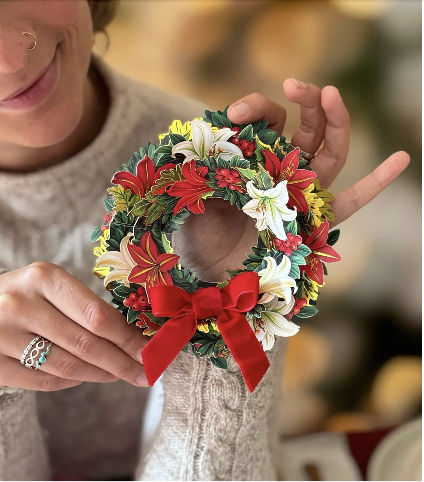 Person holding a small floral wreath with red, white flowers and a red bow.