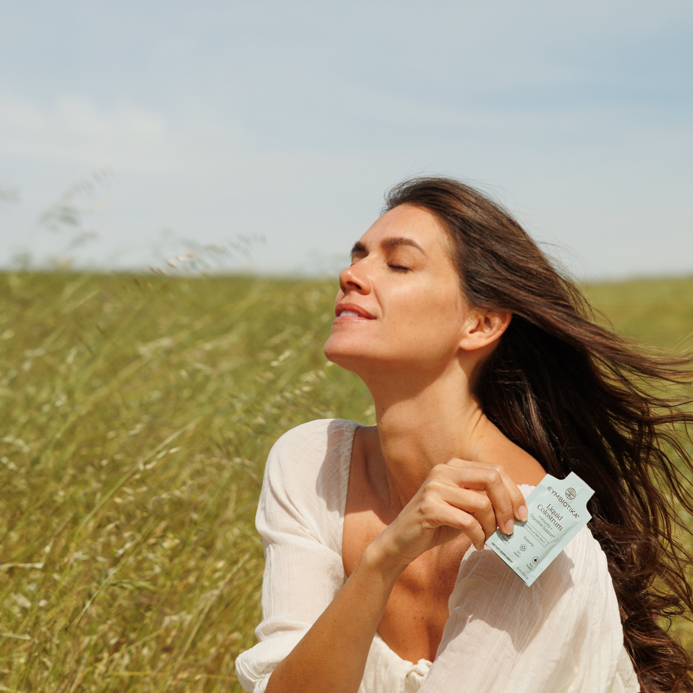 Person outdoors, eyes closed, holding a small packet in grassy field.