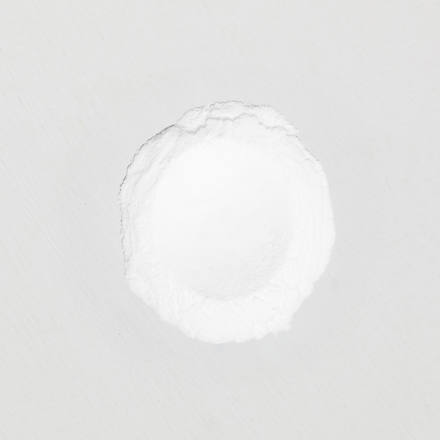 A top-down view of a circular pile of fine white powder on a white surface.