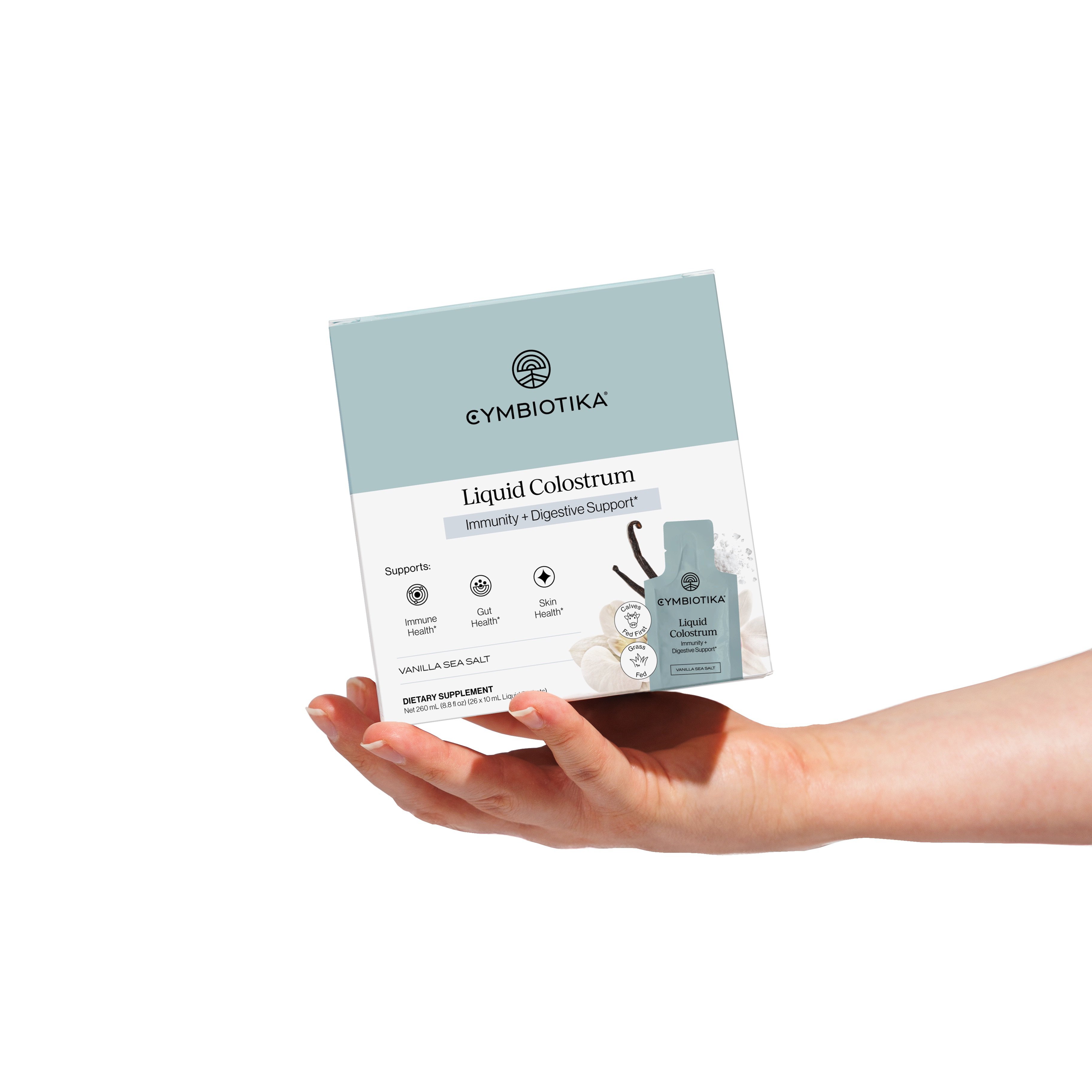 Hand holding a box labeled 'Cymbiotika Liquid Colostrum' with immunity support details.