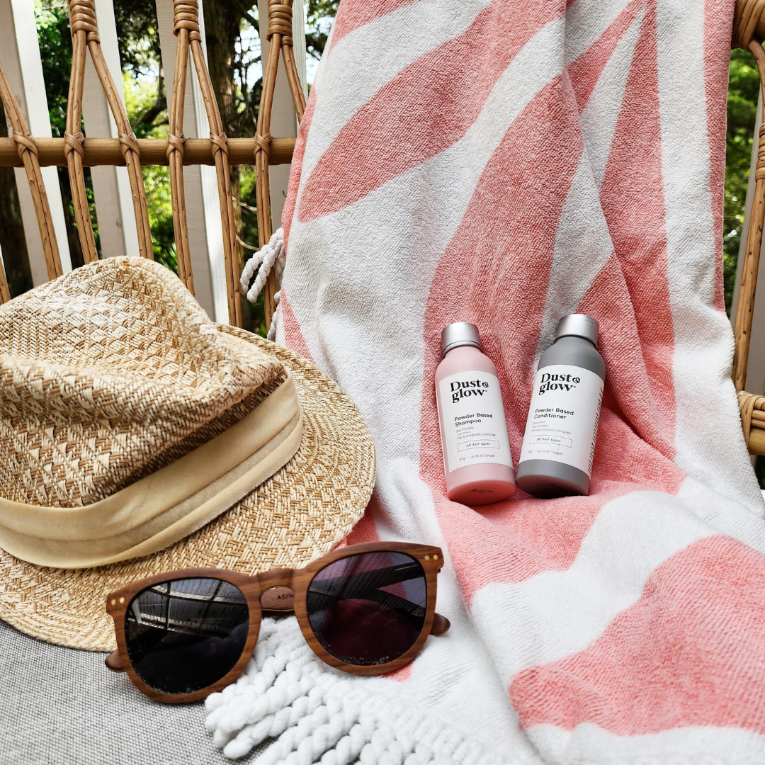 Sunglasses, a hat, and two bottles on a patterned towel.