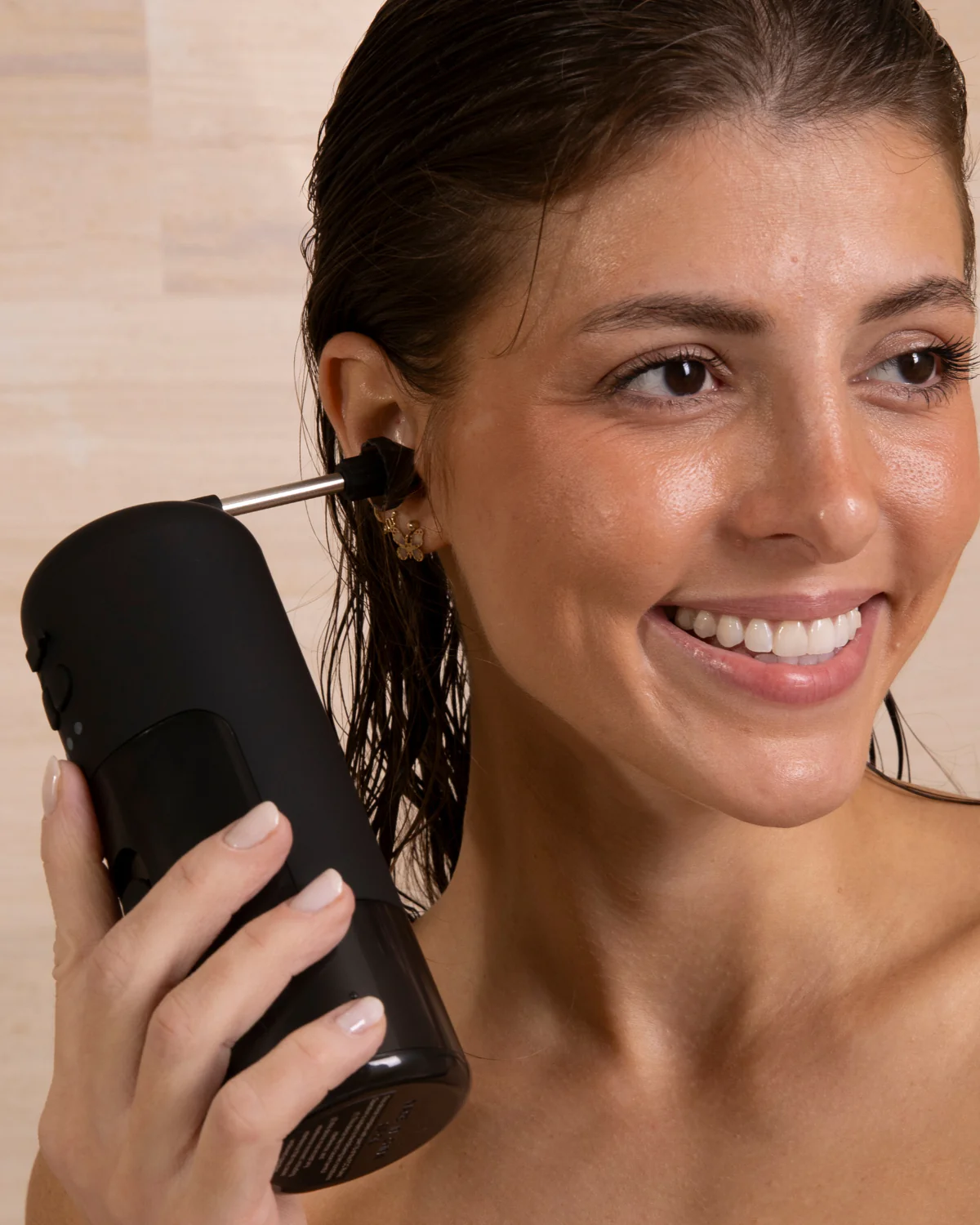 Woman using a black ear cleaning device, smiling.