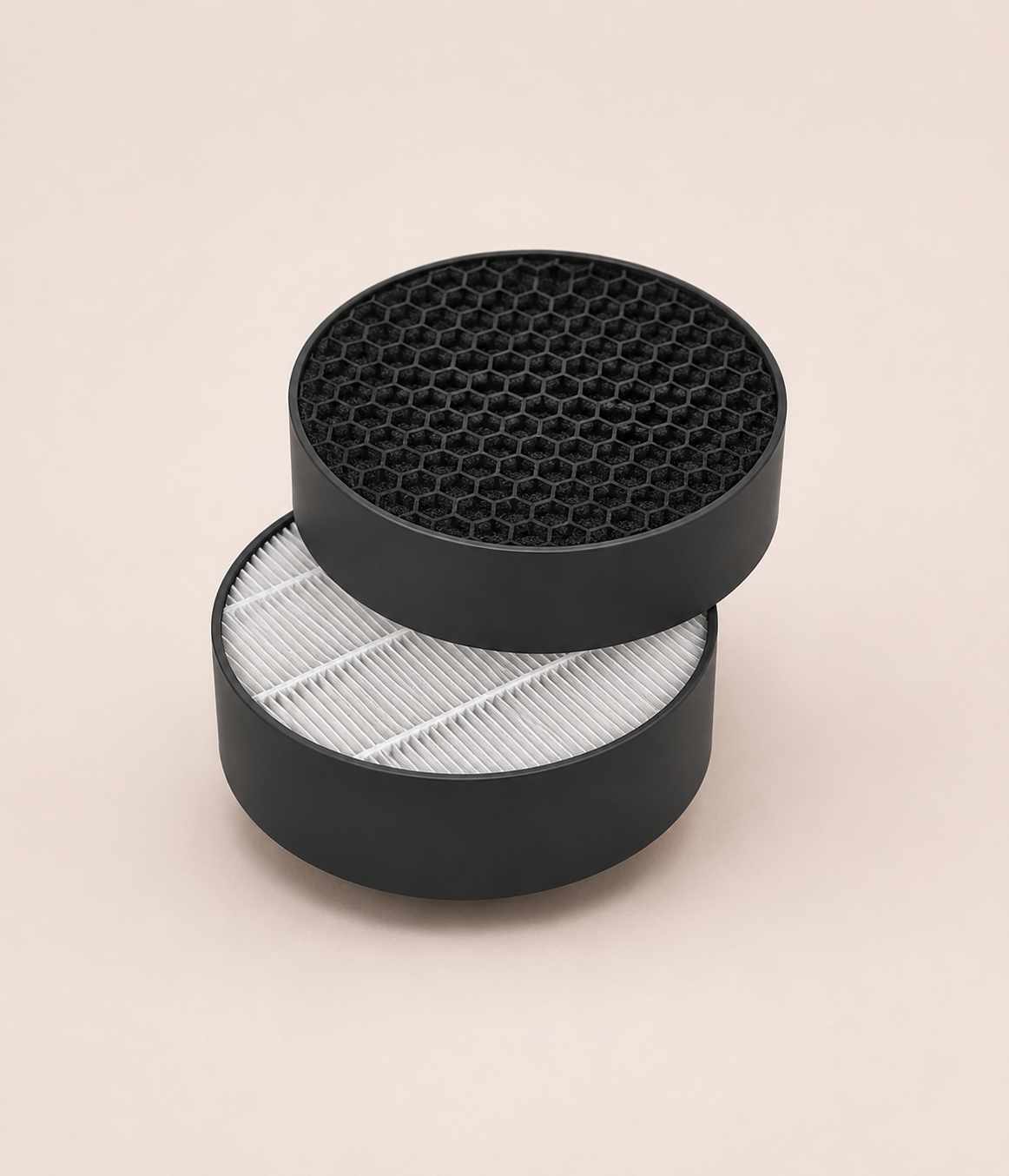 A round, black honeycomb filter sits atop a round, white pleated filter against a plain background.