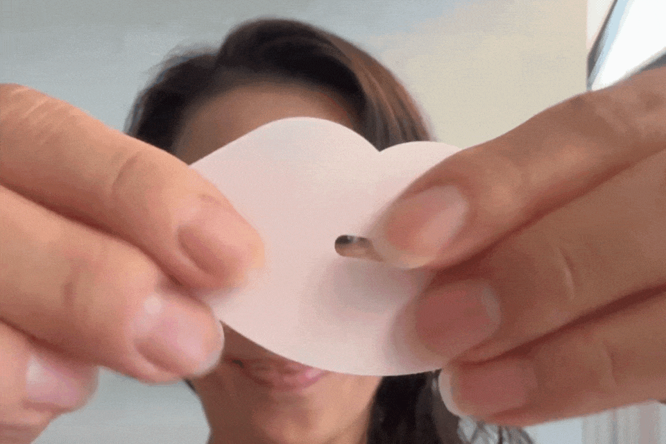 Person holding a white heart-shaped object with a small hole.