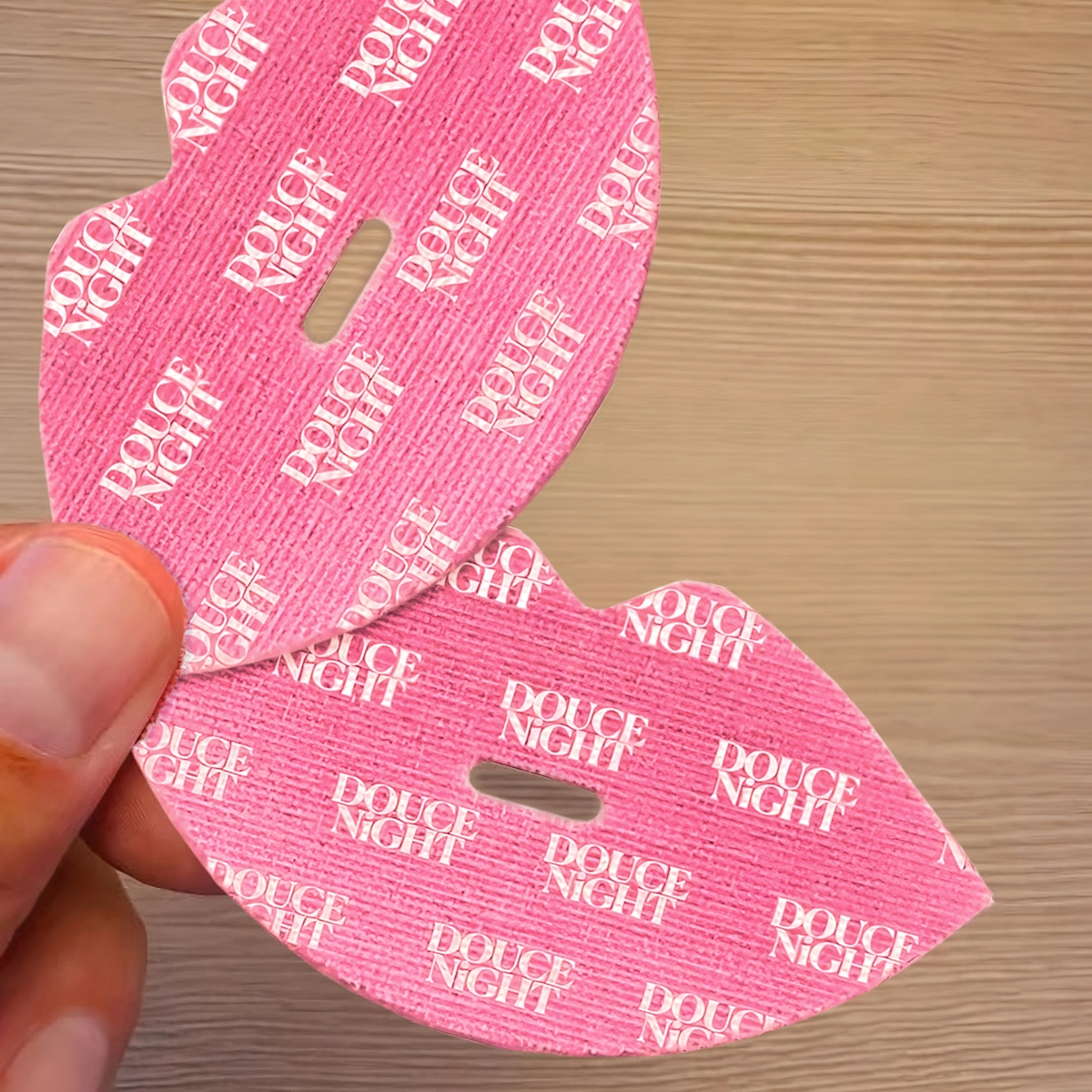 Pink lip-shaped patches with 'DOUCE NIGHT' text, held by a hand.