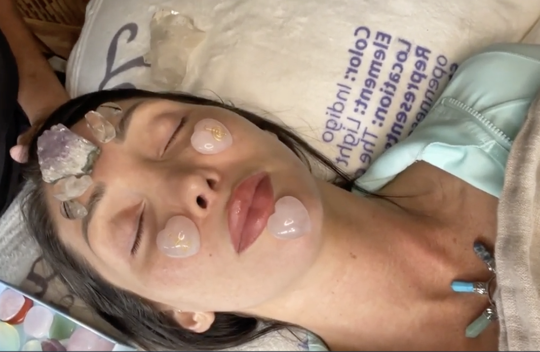 A pink mannequin bust is adorned with a rose quartz top and surrounded by various crystals.