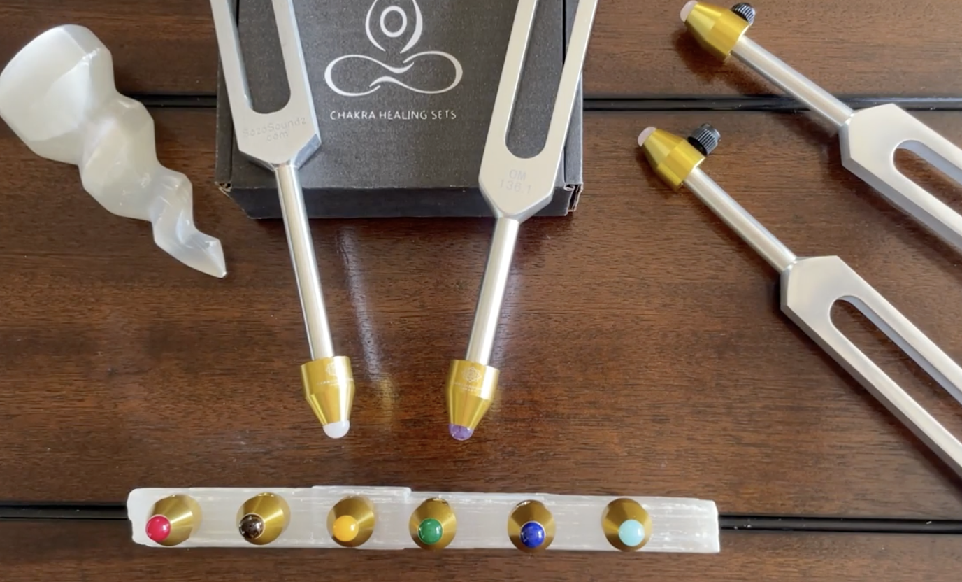 A collection of chakra healing tuning forks and crystals arranged on a wooden table.