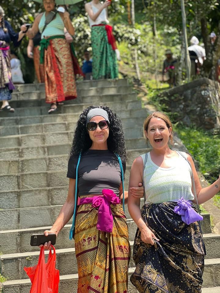 Two people wearing colorful sarongs, smiling on stone steps outdoors.