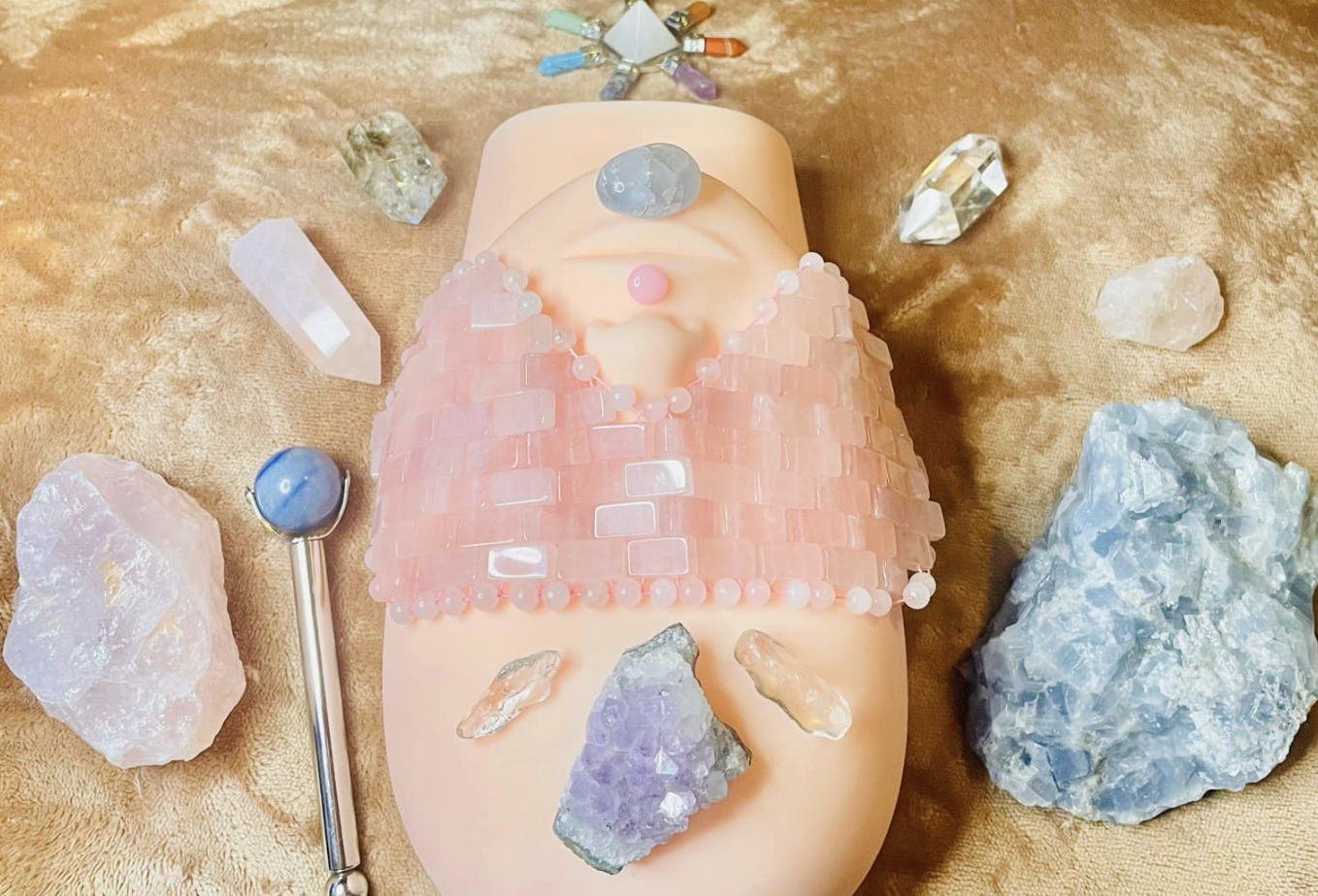 A woman lies with her eyes closed with various crystals, some heart-shaped, resting on her face.