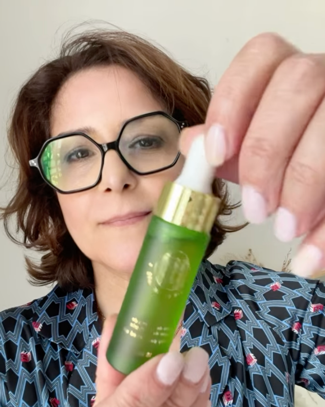 Person holding a green bottle with a dropper and gold cap.