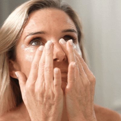 Person applying cream under eyes with fingers.