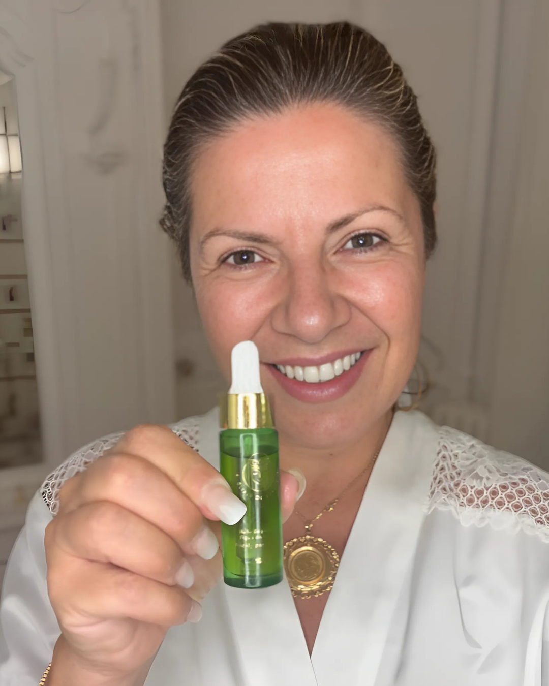 Person smiling, holding a green bottle with a dropper.