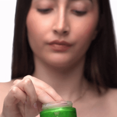 Person applying cream from a green jar.