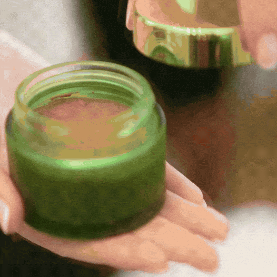 Green jar of cream held in hands.
