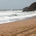 Sandy beach with waves crashing and rocky cliffs in the background.