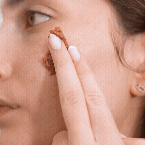 Person applying brown facial scrub to their cheek.