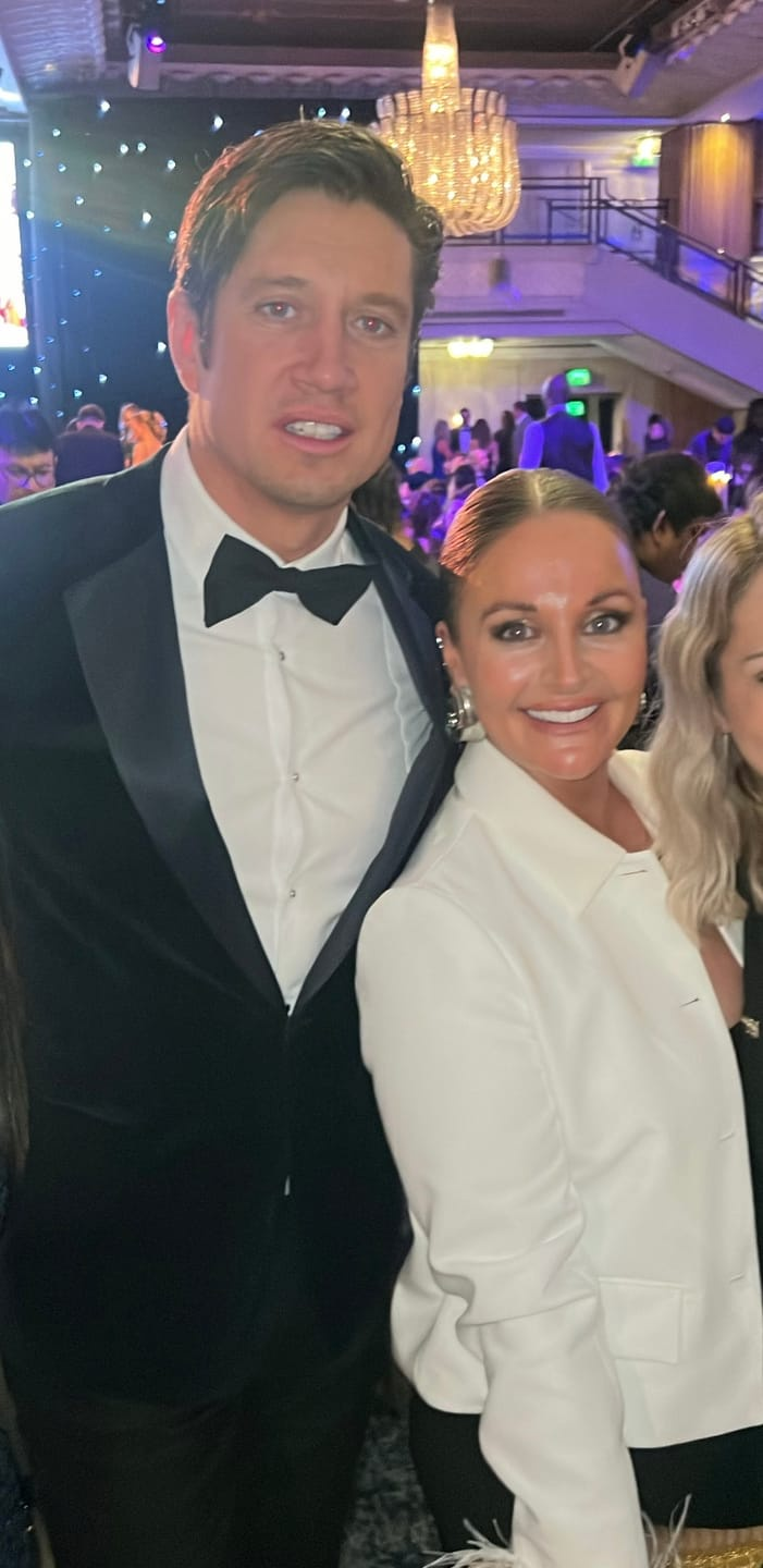 Two people dressed formally at an elegant indoor event with a chandelier.