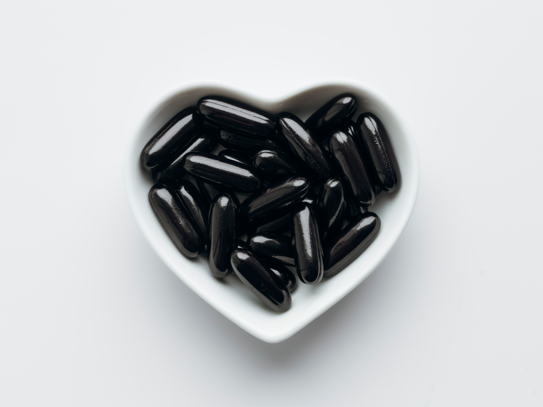 A top-down view of shiny black capsules in a white, heart-shaped bowl on a white surface.