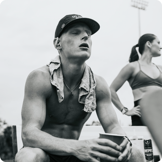 A black and white photo of a shirtless man with a towel around his neck, resting with eyes closed.