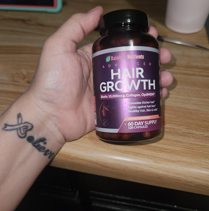Hand holding a bottle of hair growth supplements on a wooden surface.