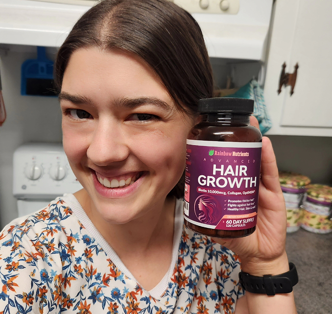 Person smiling and holding a bottle of hair growth supplements in a kitchen.