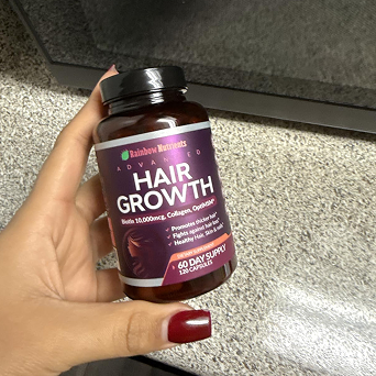 Hand holding a bottle labeled 'Hair Growth' on a speckled countertop.