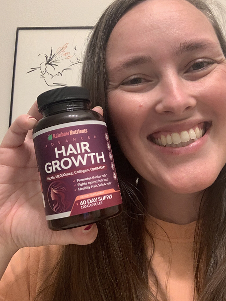 Person smiling, holding a bottle of hair growth supplements.