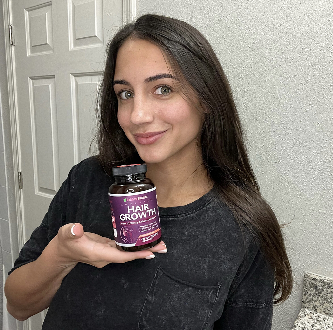 Person holding a bottle of hair growth supplements in a bathroom.