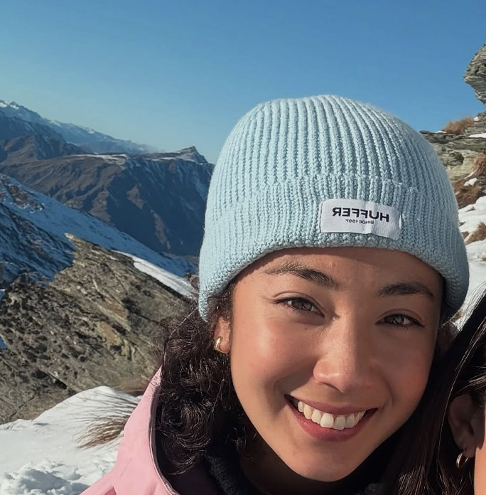 Person in a blue beanie smiling with snowy mountains in the background.